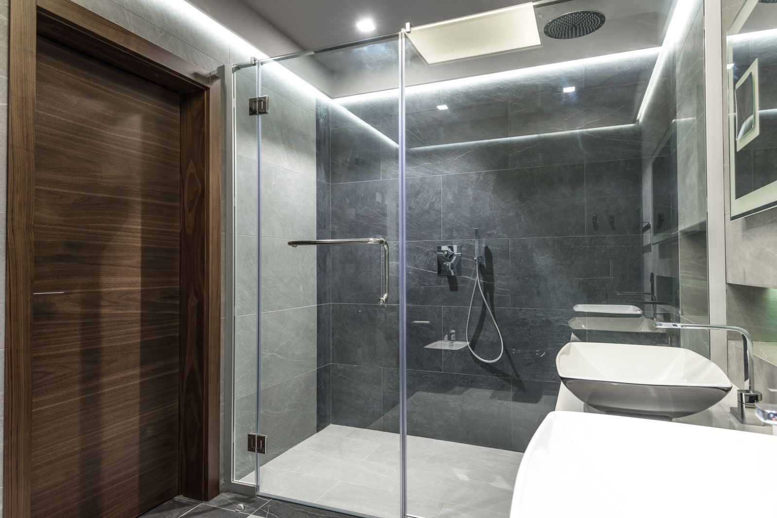 A frameless glass walk-in shower in a dark stone bathroom