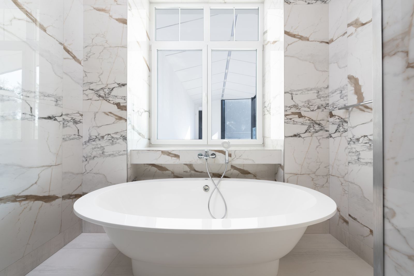 A low-lit primary ensuite with a freestanding tub against a marble feature wall